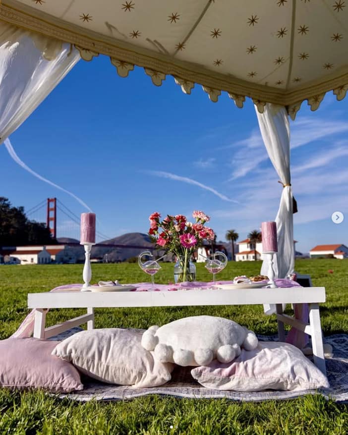 Romantic setting for two of a short table, over a blanket outside with a tent covering it. Candles, pillows and flowers by Mellow Events